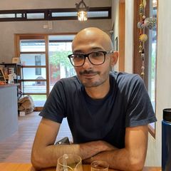 A handsome, bald man with coffee coloured skin sitting at a table smiling.