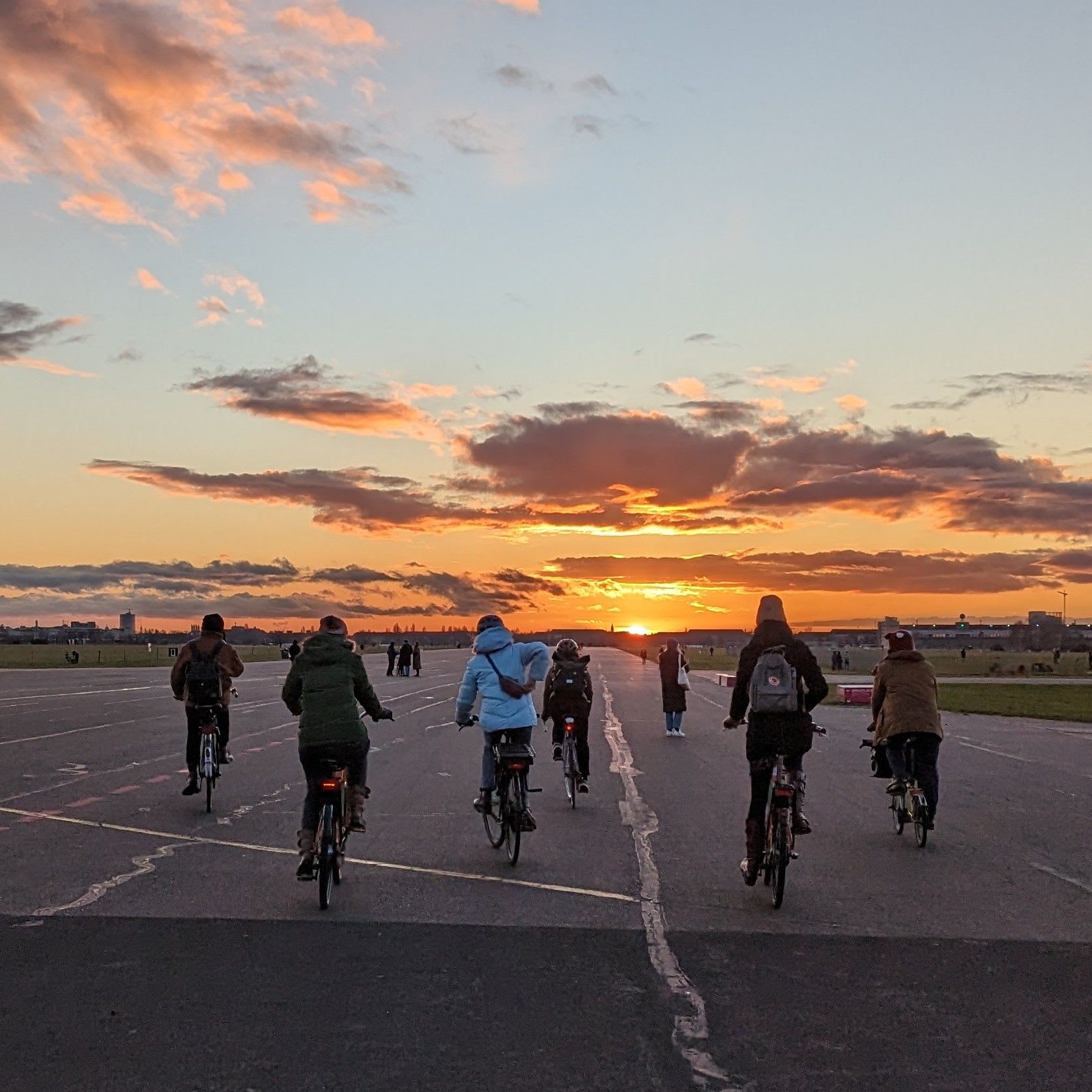 6 people riding into the sunset on a wide tarmac.