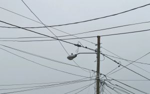 Mess of telephone and electric wires coming off an electric pole with light.
