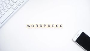 Letter tiles spelling out 'WordPress' positioned between a mobile phone and a laptop.