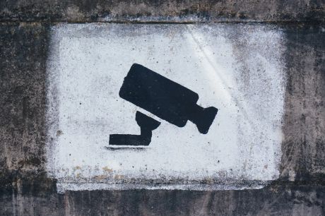 Graffiti art of a black security camera painted in a white frame.