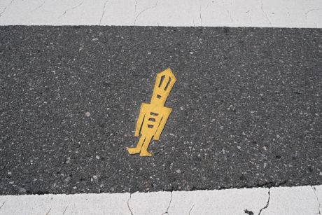Yellow sticker of elongated person on grey concrete pathway.